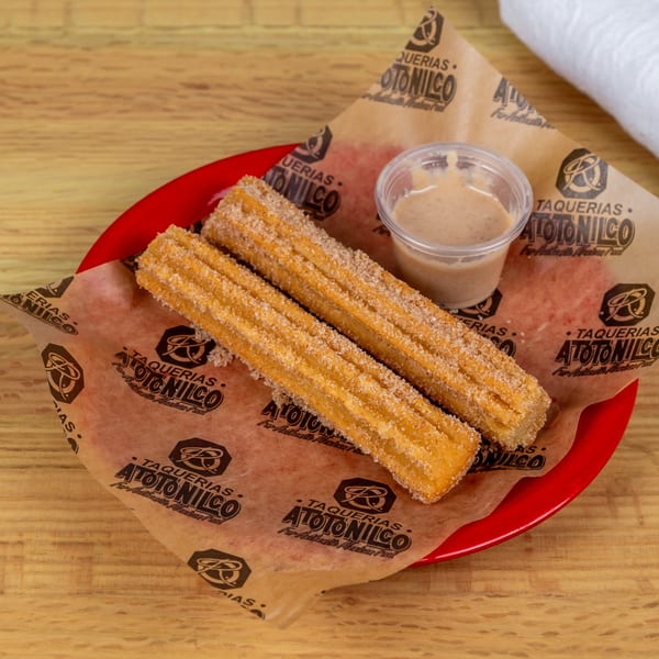 Two sugar-dusted churros and a cup of dipping sauce on Taquerias Atotonilco branded paper.
