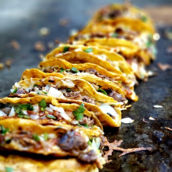 A row of delicious Taquerias Atotonilco tacos with meat, onions, and cilantro on a griddle.