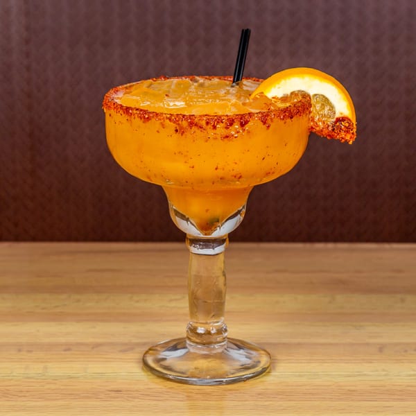 A mango margarita with a chili-lime rim and orange slice, on a wooden table.