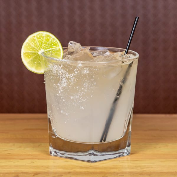 A refreshing margarita with a salted rim, lime slice, and black straw, on a wooden table.