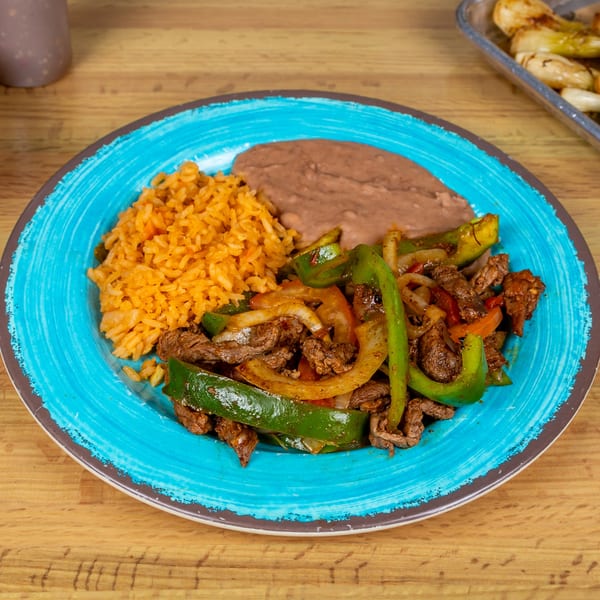 Taquerias Atotonilco's fajitas with steak, bell peppers, onions, rice, and refried beans on a blue plate.