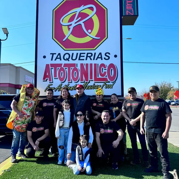 A group of people, including children, pose in front of the Taquerias Atotonilco sign.