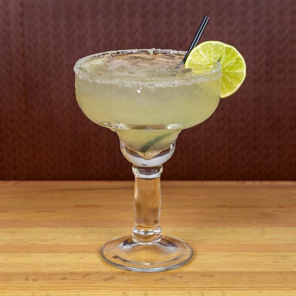 A salt-rimmed margarita with a lime wedge and black straw, on a wooden table.