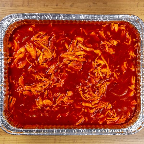 Shredded chicken in a rich red sauce, served in a large aluminum catering pan.