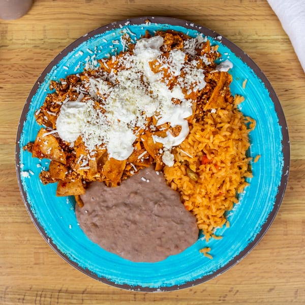 A vibrant blue plate of chilaquiles with sour cream and cheese, served with rice and refried beans.