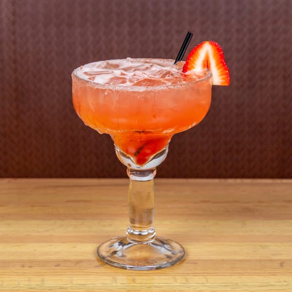 A strawberry margarita with a salted rim and a strawberry garnish on a wooden table.