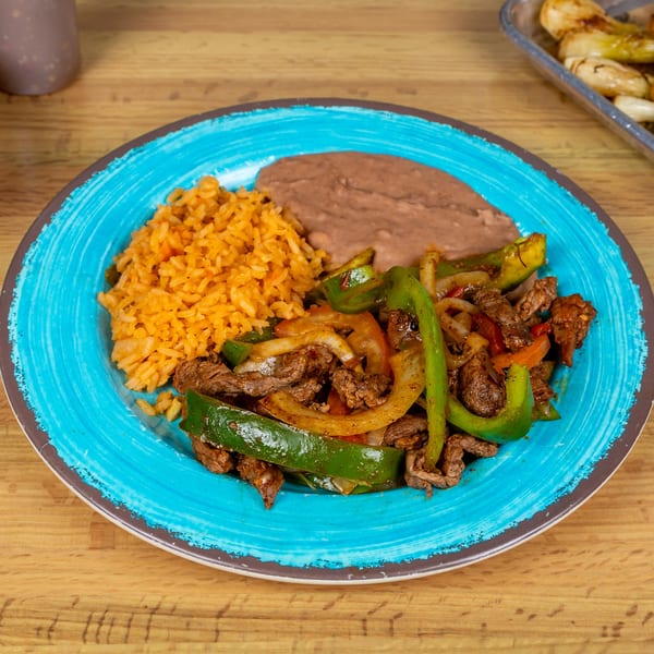 Fajitas with steak, peppers, and onions, served with Mexican rice and refried beans on a blue plate.