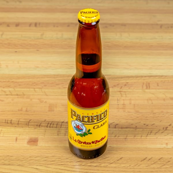 A bottle of Pacifico Clara beer with a yellow label and cap, on a wooden table.