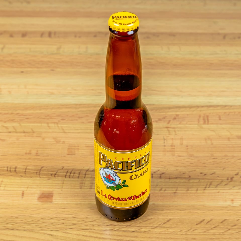 A bottle of Pacifico Clara beer with a yellow label and cap, on a wooden table.