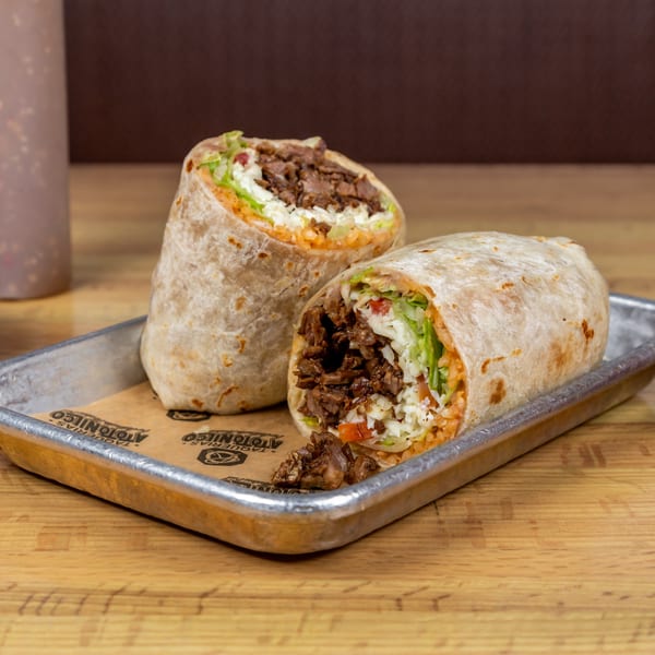 Two large burritos, one cut in half, filled with meat, rice, lettuce, and cheese on a metal tray.