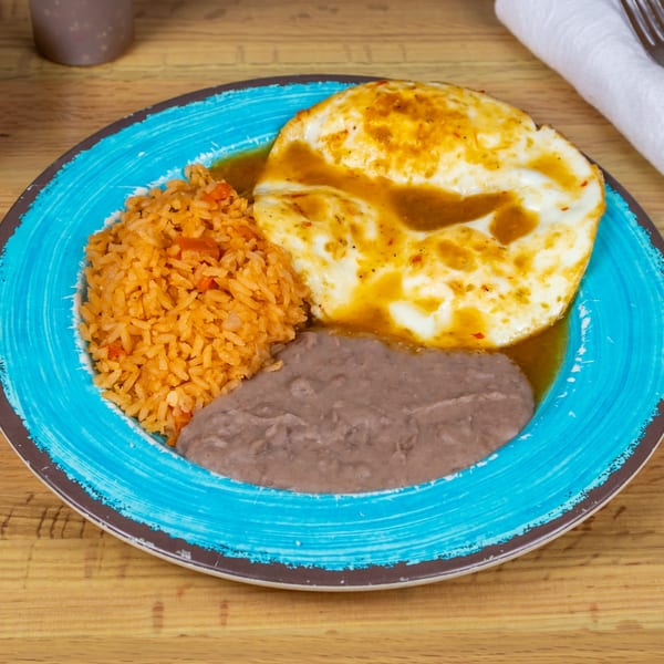 Huevos Rancheros with two fried eggs, rice, and refried beans on a blue plate.