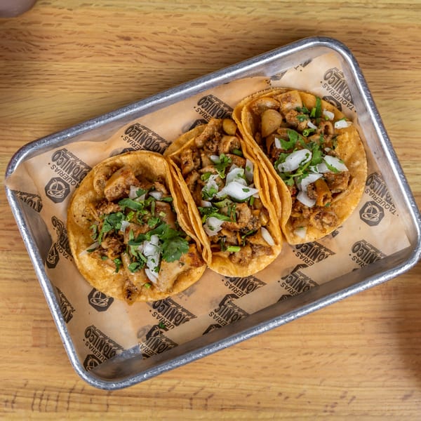 Three Taquerias Atotonilco tacos with meat, onions, and cilantro on a metal tray.
