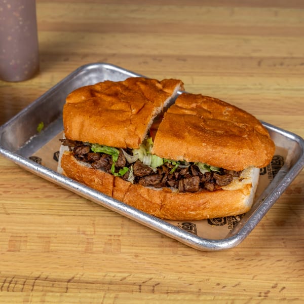 A large Mexican torta sandwich, cut in half, filled with meat and lettuce on a metal tray.